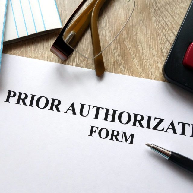 Prior authorization form with pen, calculator and glasses on desk